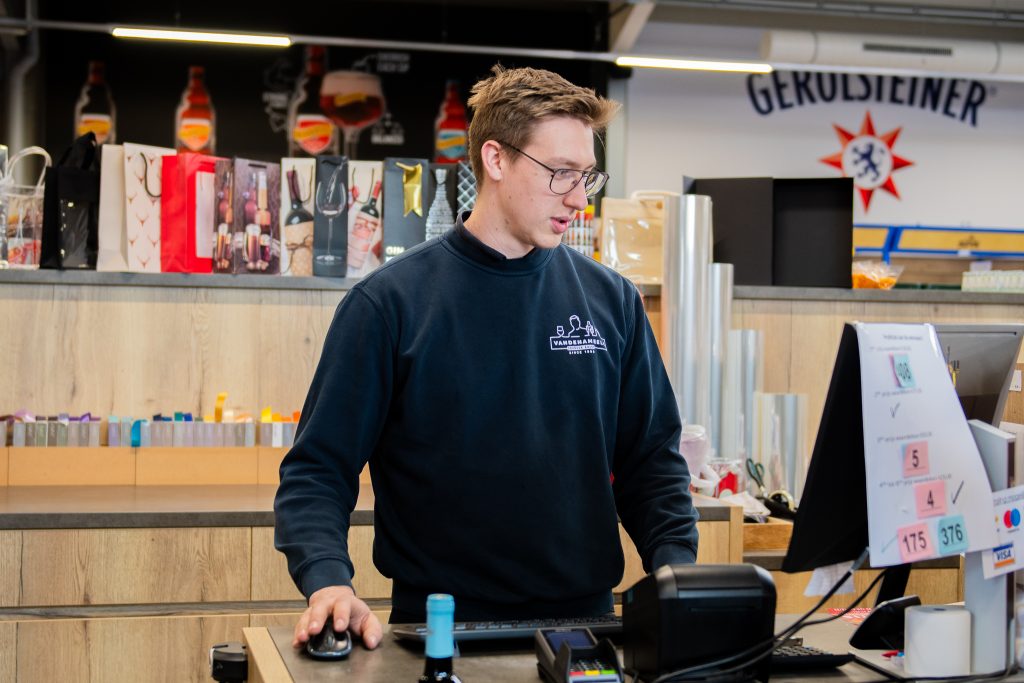 Winkelmedewerker van Dranken Vandenameele aan de kassa in de drankenwinkel.