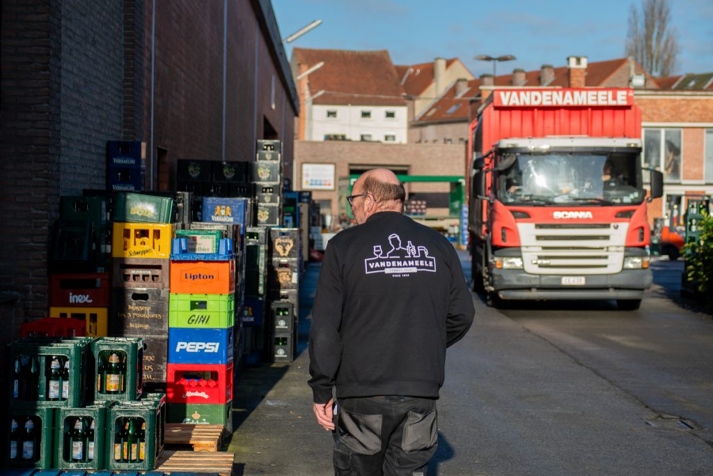 Medewerker van Dranken Vandenameele op de laadplaats naast drankkratten en een rode leveringsvrachtwagen.