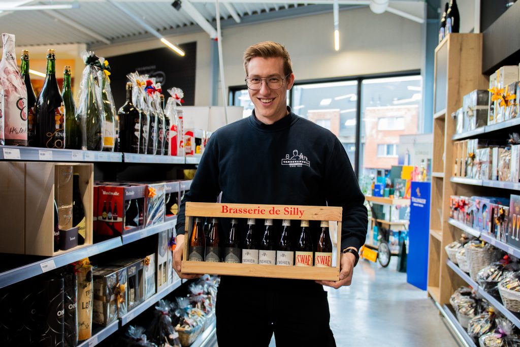 Medewerker van Dranken Vandenameele toont een houten bierpakket van Brasserie de Silly in de winkel.
