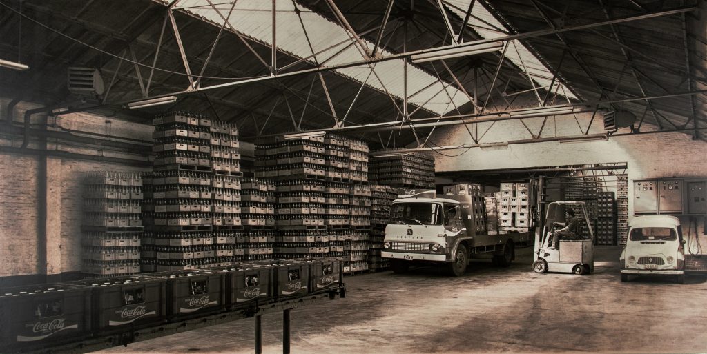 Historische foto van het magazijn van Vandenameele met Coca-Cola kratten en vrachtwagens in de jaren na de Tweede Wereldoorlog.